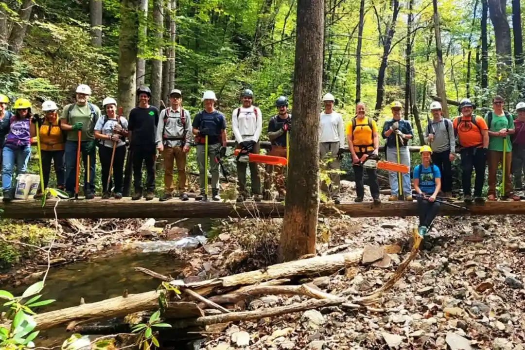 A trail work crew stands on a log